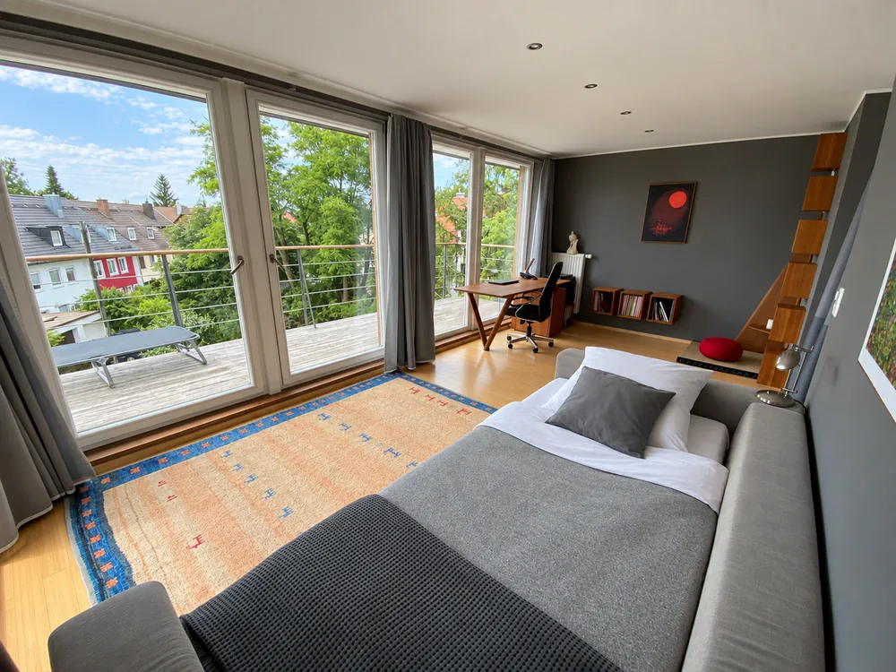 Oberes Zimmer mit Bett, Sofa und Fensterfront
